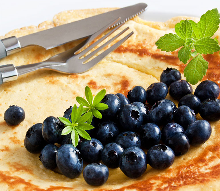 Pancakes with fresh blueberries, mint leaves, and cutlery on a light-colored plate