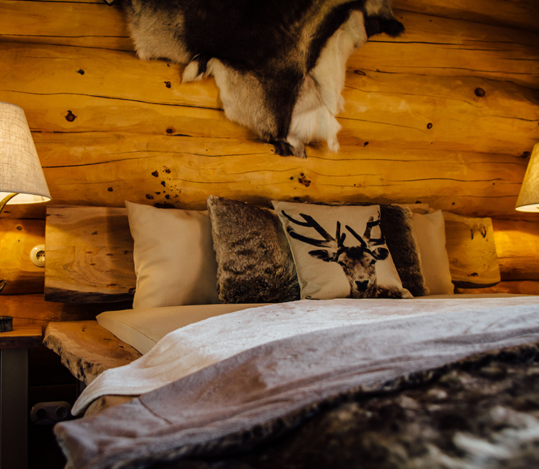  A bed with a fur throw in a log cabin suite featuring reindeer hide on the wall and leather armchairs