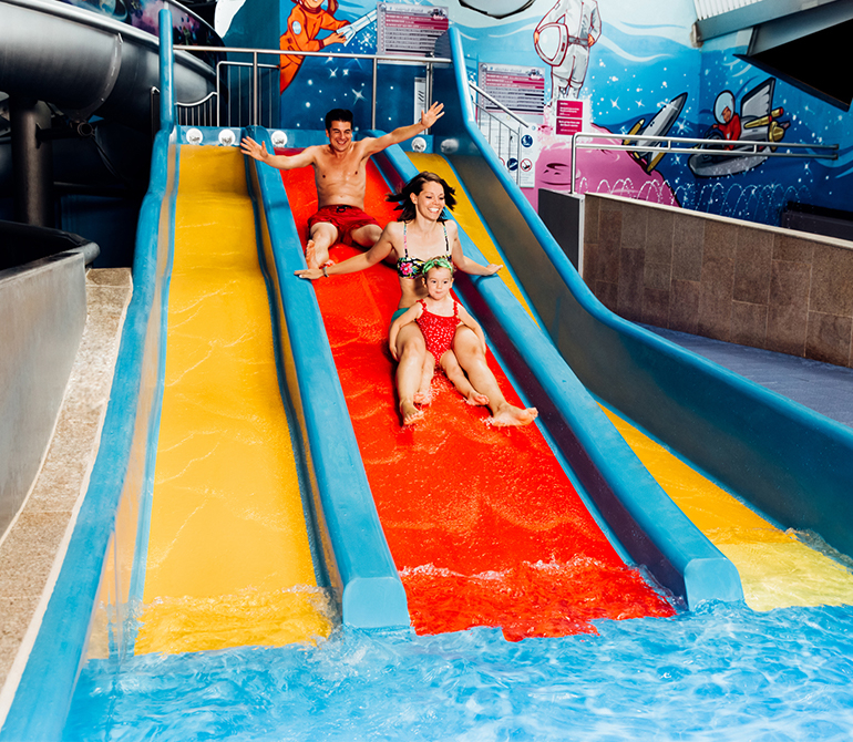 Family sliding down a colorful water slide with three lanes.