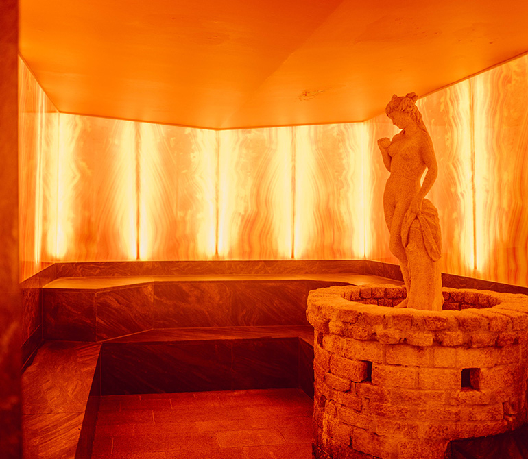 Orange-lit sauna in onyx stone look with a sauna heater in the center.