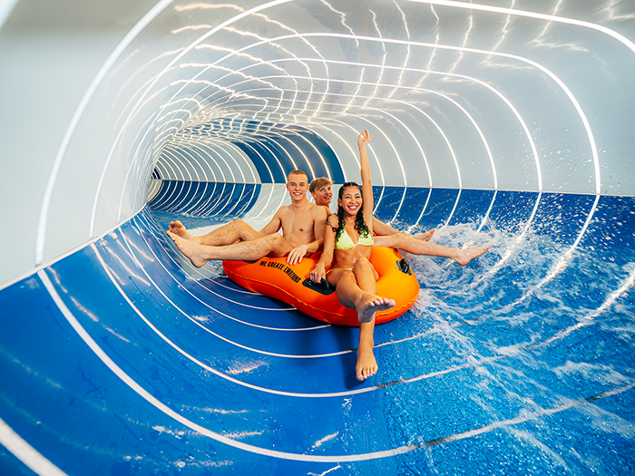 Three teenagers slide down the blue and white striped tube slide on a tire.