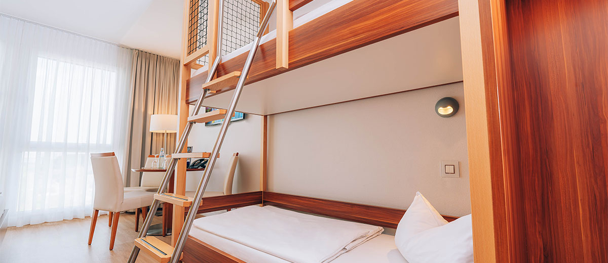 Hotel Victory Therme Erding Bellezza Side view of a bunk bed and a ladder to the upper bed. In the background a table with chairs