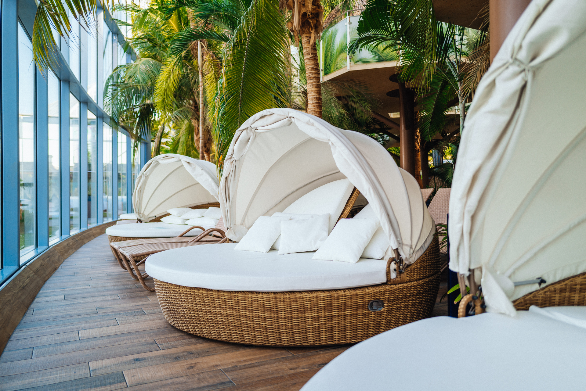 Eine Liege aus Rattan mit weißer Liegefläche und Kissen unter Palmen.