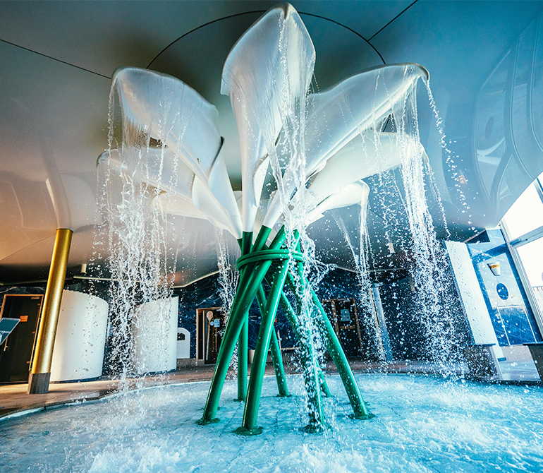A waterfall installation shaped like white calla lilies, with water flowing from the petals into a basin inside the Erding Thermal Baths