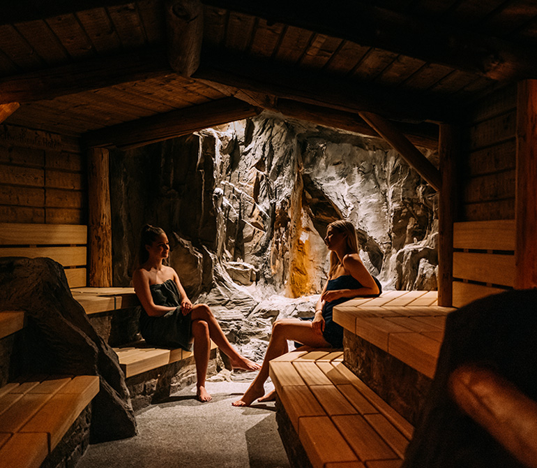 Zwei Frauen in Bademänteln sitzen in einem holzverkleideten Sole-Stollen mit Felswänden in der Therme Erding
