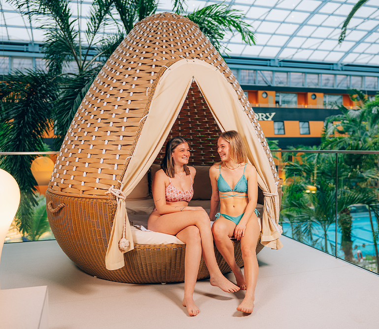 Zwei Frauen entspannen gemeinsam auf einer verschließbaren Rattan-Liege in Kokosnussoptik.