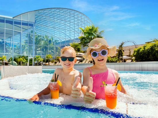 Zwei Kids mit Sonnenbrille sitzen mit einem Getränk im Pool. 