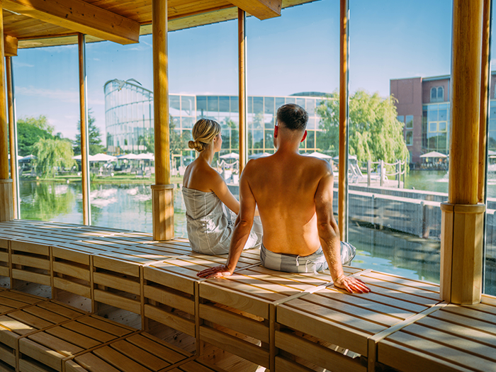 A couple sits in a sauna with a large glass front and enjoys the view.