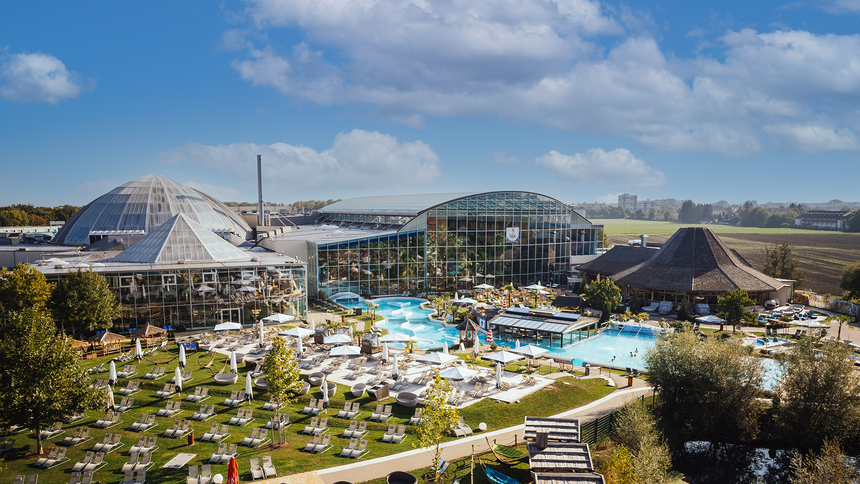 Luftaufnahme des Thermengartens der Therme Erding mit Pools, LiegestĂŒhlen und GebĂ€uden unter blauem Himmel