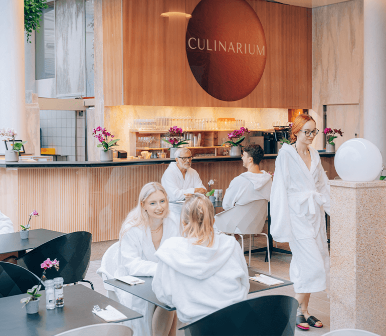 A seating area with tables and chairs next to a pool, situated under a large glass dome filled with tropical plants in the spa restaurant