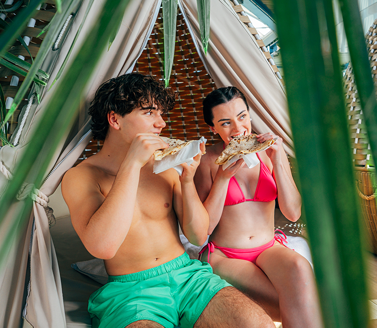 A girl and a boy are eating delicious crepes, surrounded by palm trees.