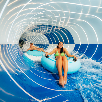 Two guests slide down a water slide on a tire.
