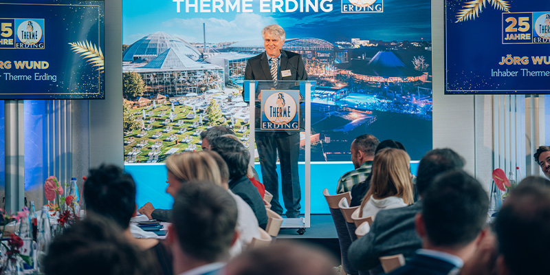 Mann am Rednerpult bei Pressekonferenz zum 25-jährigen Jubiläum der Therme Erding, Publikum im Vordergrund