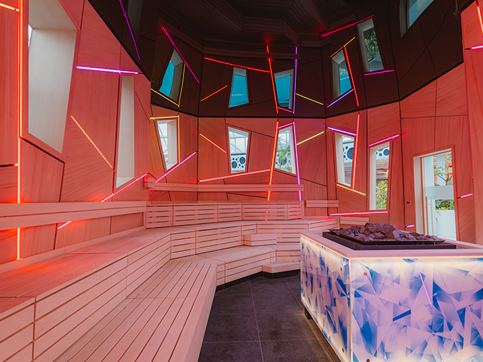 A sauna with wooden benches, surrounded by colorful neon lights, with a sauna stove in the center.
