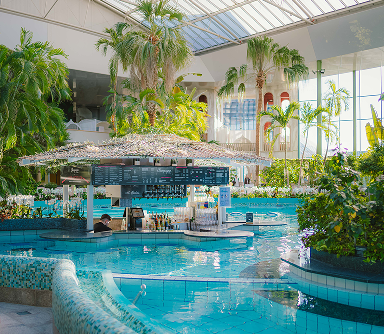 Pool bar with a canopy of green leaves at the VitalTherme in Therme Erding, surrounded by water and palm trees