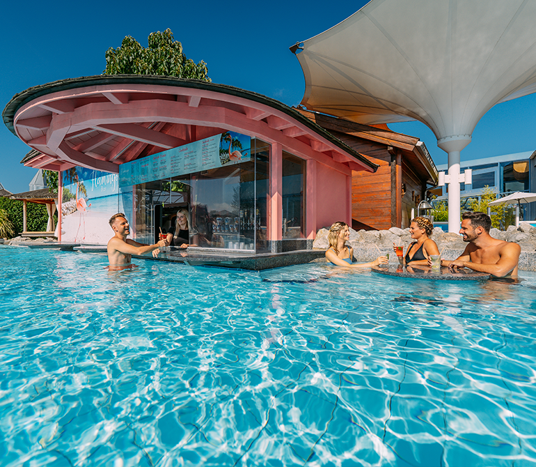 People are enjoying drinks at a pink pool bar while sitting in the water on a sunny day