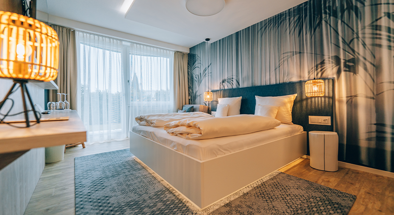 Modern room, brightly furnished in grey tones, view of a double bed and a small lamp that provides cosy light