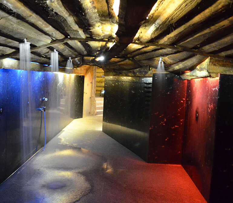 Showering with water jets in a tunnel featuring a wood-paneled vaulted ceiling and colored lighting at the Erding Thermal Baths