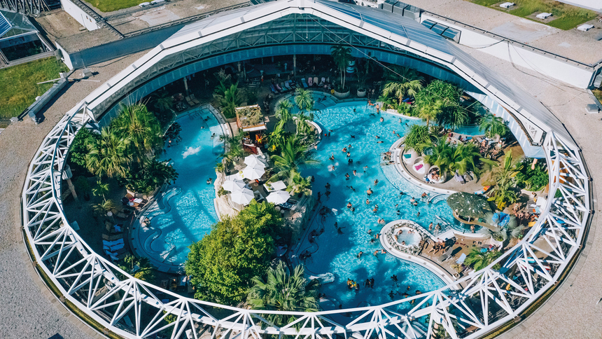 Luftaufnahme des kreisförmigen Außenbeckens der Therme Erding mit Schwimmenden und grüner Bepflanzung