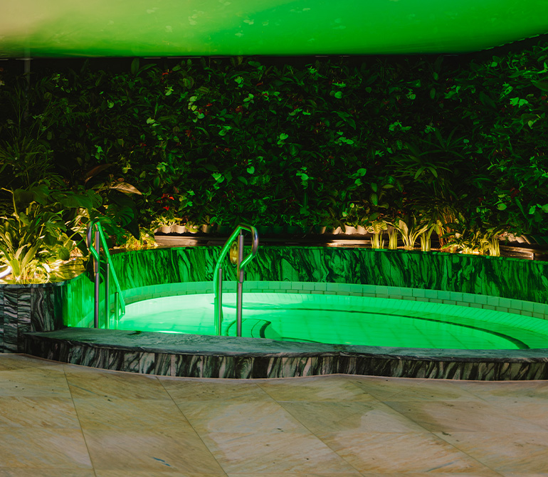 Round pool with green lighting, surrounded by green plant walls.
