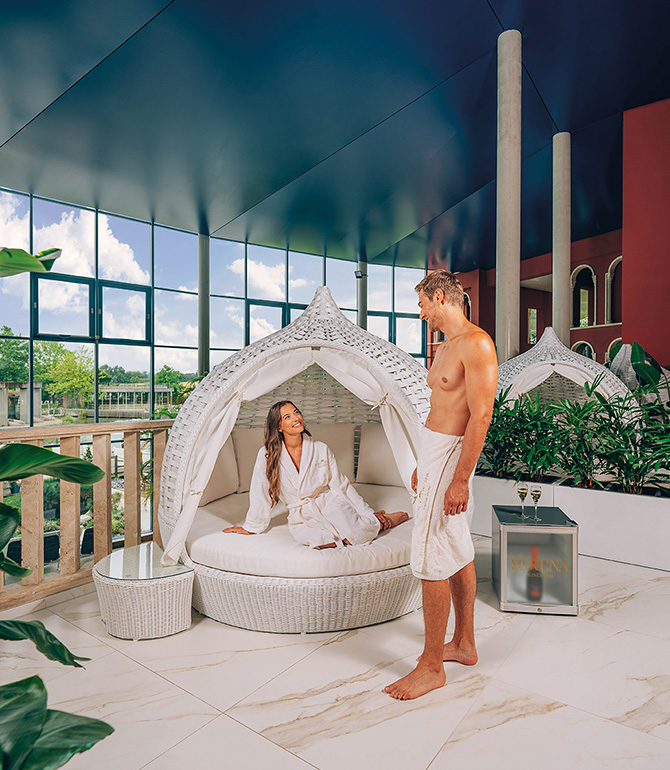 A woman and a man in a private lounge. It features a private sleeping area, a personal refrigerator, and a small table.
